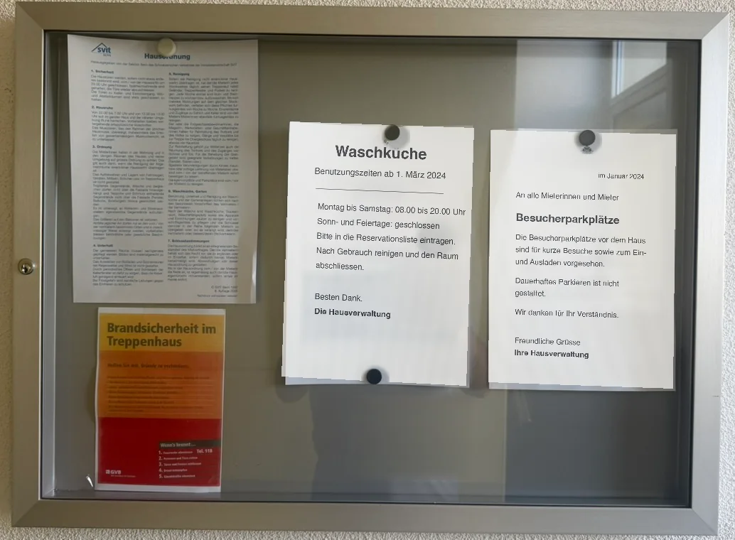 Klassisches Anschlagbrett im Treppenhaus, Papier-Aushänge hinter Glas